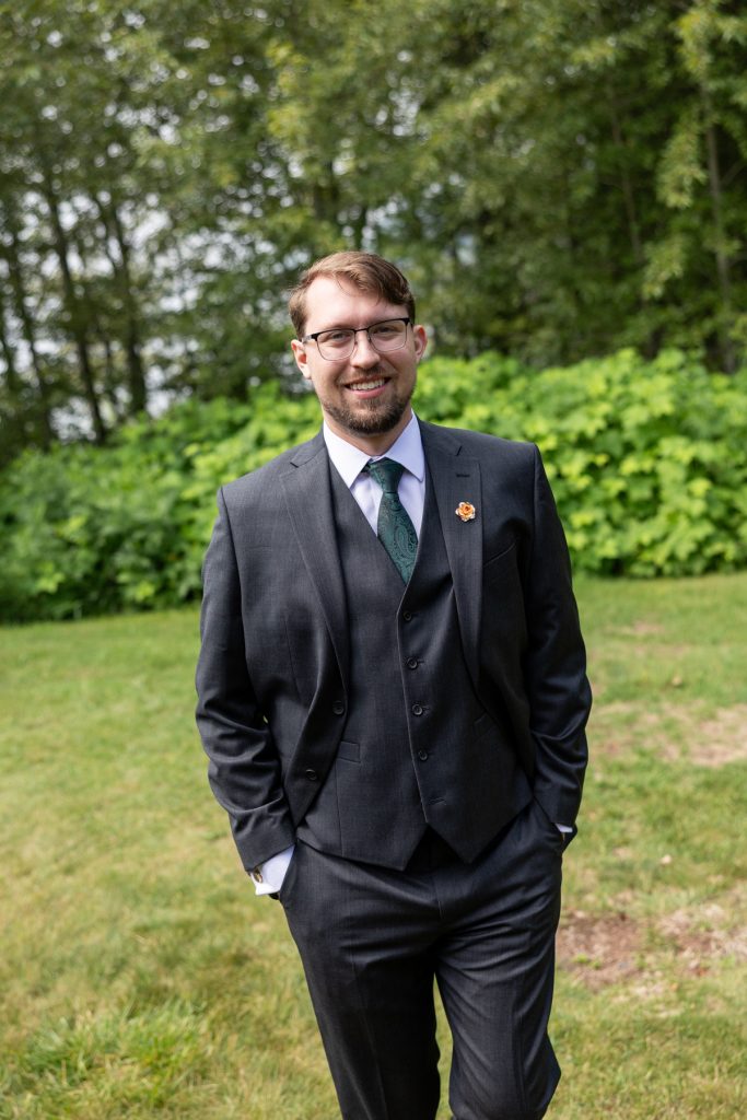 Groom in a gray suit and green tie smiles confidently outdoors, showcasing wedding photography services