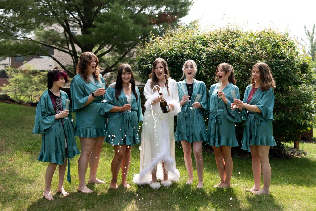 Bride and her bridesmaids celebrating with champagne in matching teal robes, capturing joyful moments