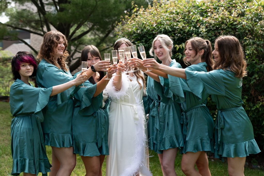 Bride and bridesmaids in matching teal robes toasting with champagne glasses, captured by Beau Petersen