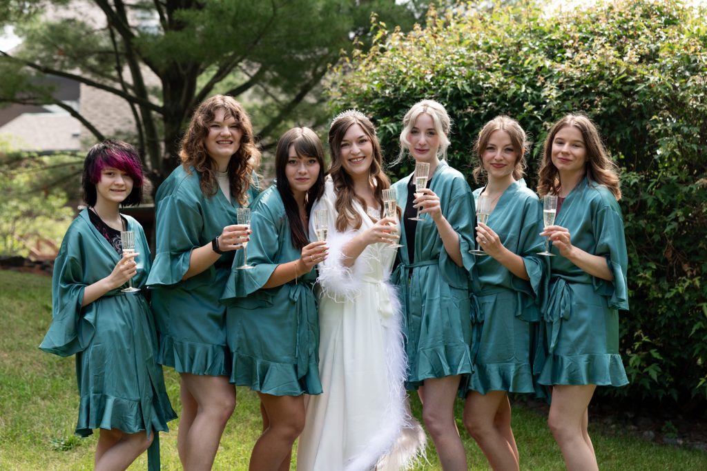 Bride and bridesmaids in green robes toasting with champagne at a Wisconsin wedding, captured