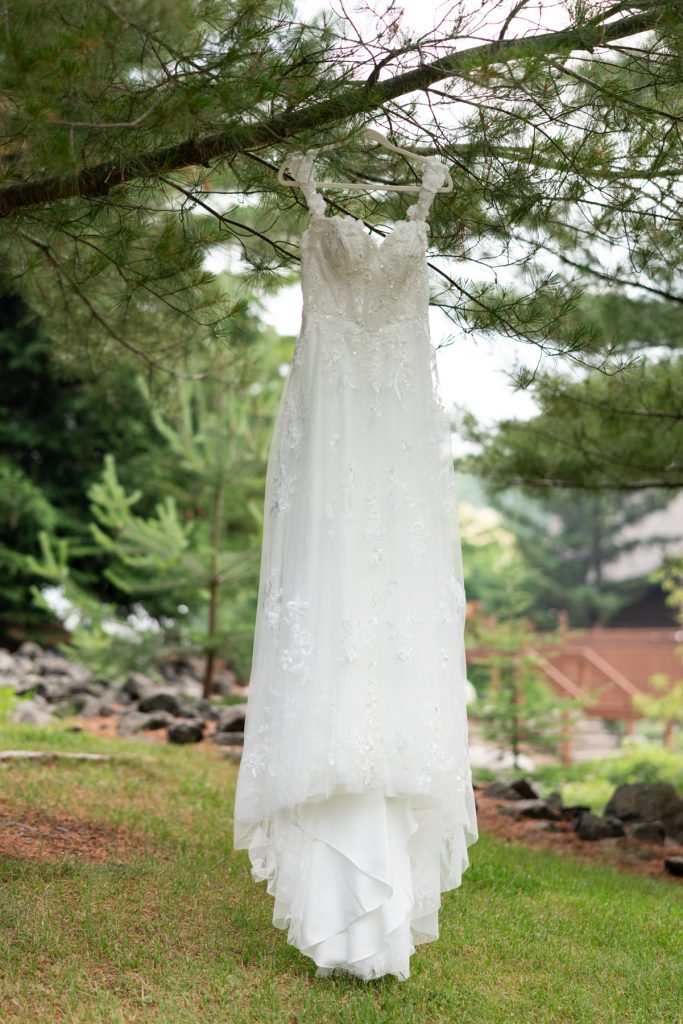 Elegant white wedding dress hangs from a tree branch in a lush, green outdoor setting