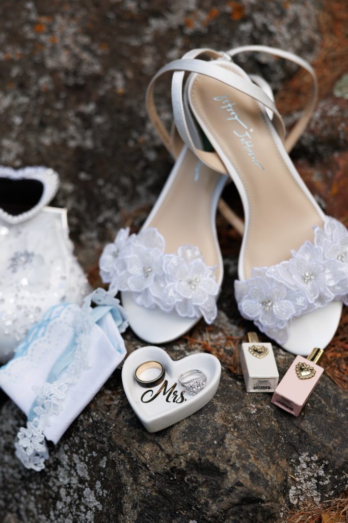 Elegant wedding details including white sandals, a sparkling garter, and wedding rings displayed