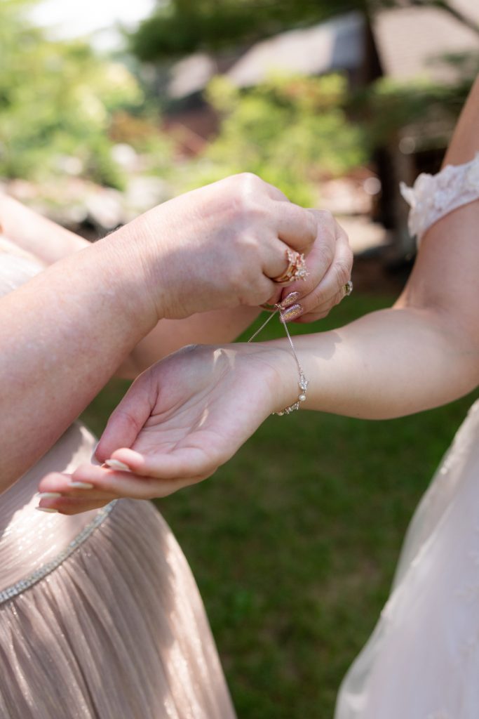 Close-up of a wedding detail showing a bridesmaid assisting the bride with a delicate bracelet