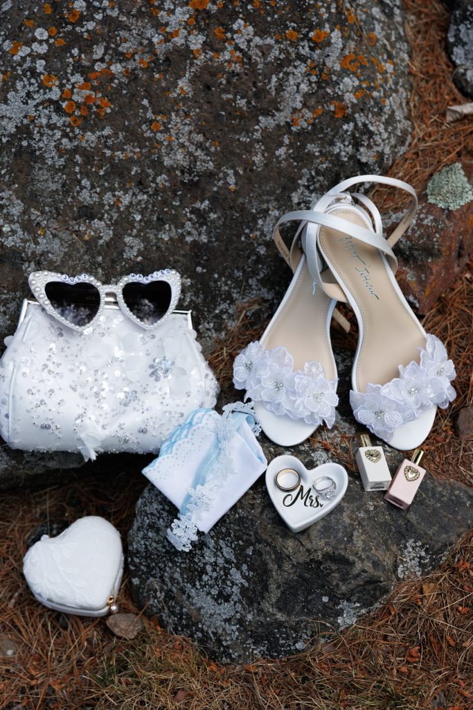 Elegant silver sandals, a sparkling heart-shaped clutch, and delicate wedding accessories arranged on a textured