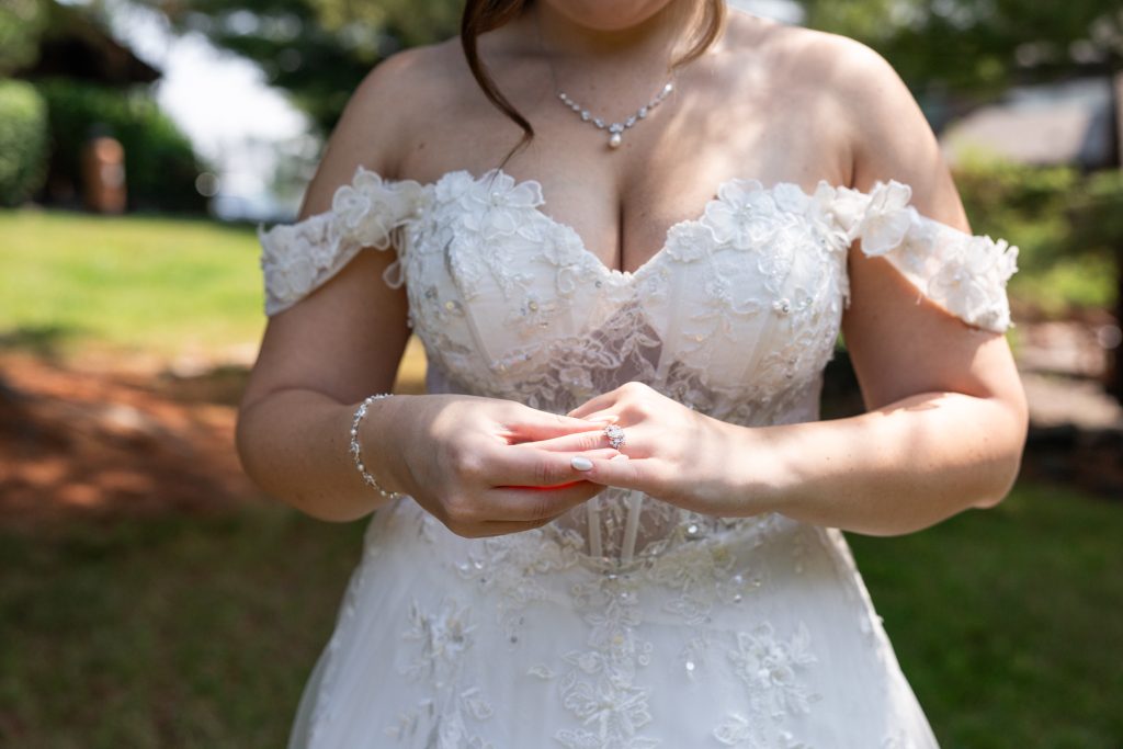 Bride in an off-the-shoulder wedding dress admires her engagement ring in a Wisconsin outdoor setting