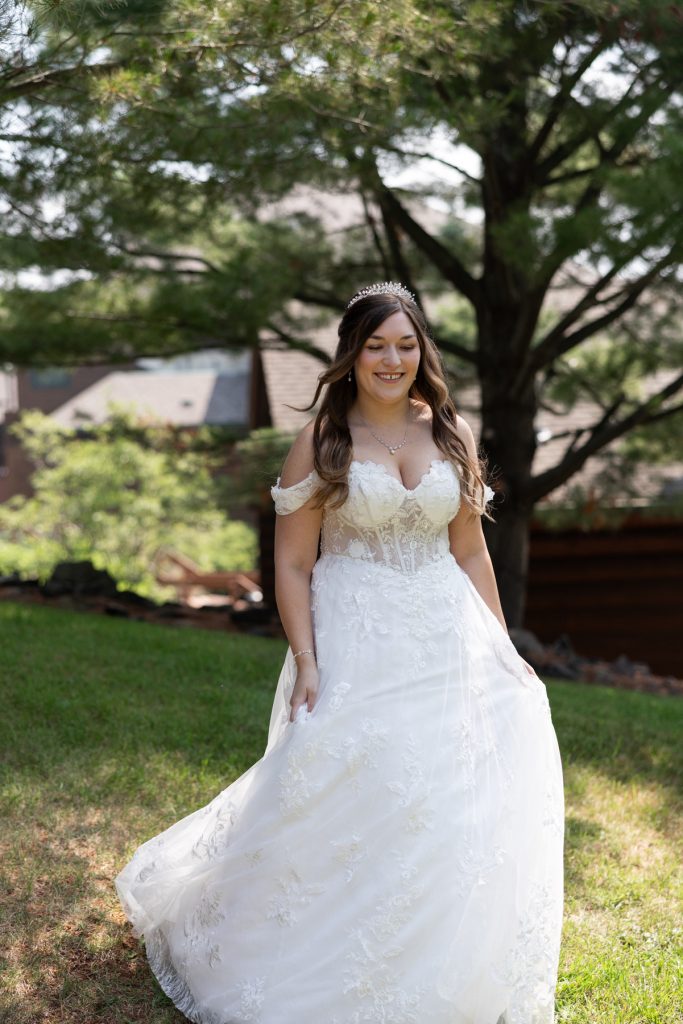 Bride in a detailed lace wedding dress and tiara smiles outdoors in a Wisconsin garden