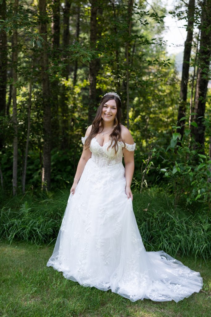 Bride in a white lace wedding dress poses in a lush, green forest setting, showcasing