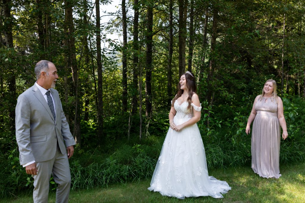 Bride in a flowing wedding dress smiles at groom during a first look moment