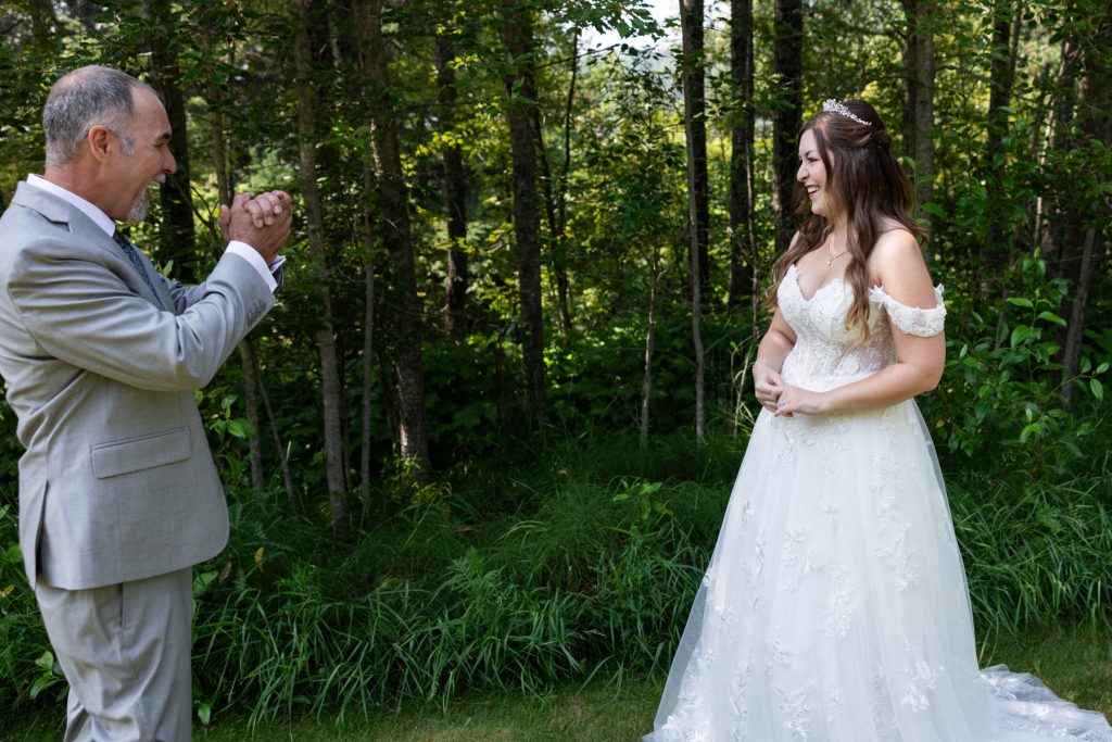 Bride and groom sharing a joyful first look moment in a wooded setting, captured