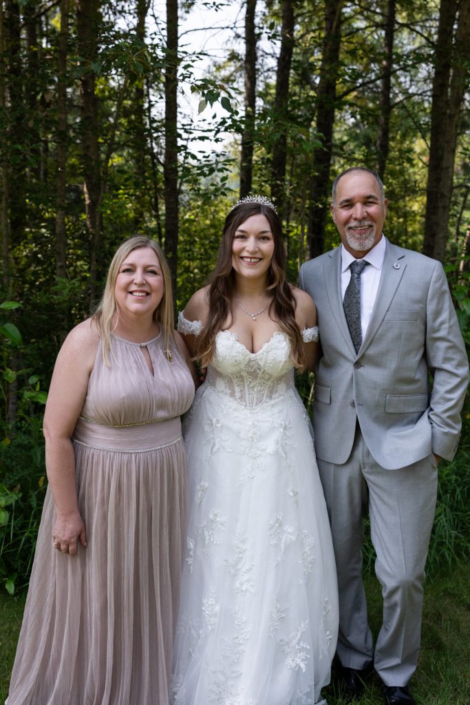 Bride stands between her parents in a formal portrait during a Wisconsin wedding photography session