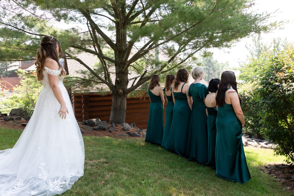 Bride in wedding dress looking toward bridesmaids in green dresses at a Wisconsin wedding, captured