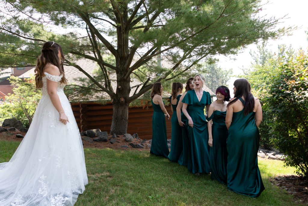 Bride in a white wedding dress looks toward her bridesmaids in emerald green dresses