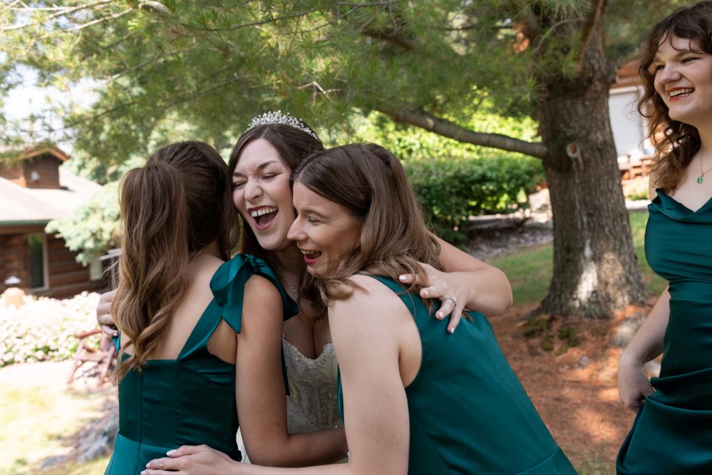 Bride laughing with bridesmaids in green dresses during a joyful wedding celebration in Hayward, Wisconsin.