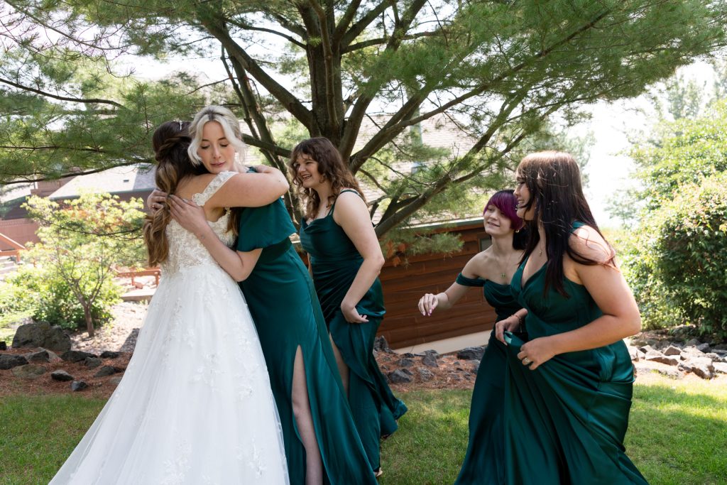 Bride in a white wedding dress embraces bridesmaids in emerald green dresses, captured