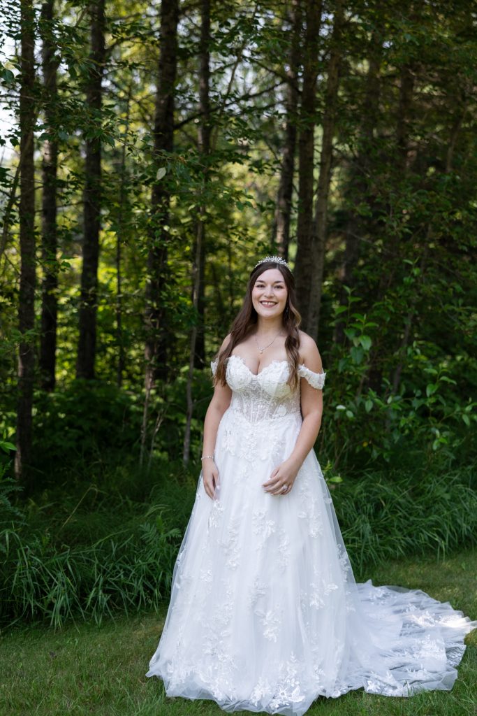 Bride in a detailed lace wedding gown stands outdoors in a wooded setting, showcasing Wisconsin