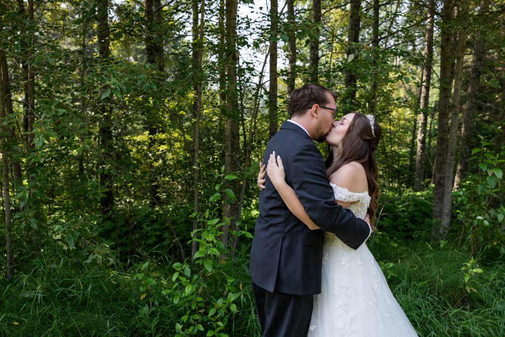 Bride and groom share a tender kiss embraced in a lush forest setting, captured