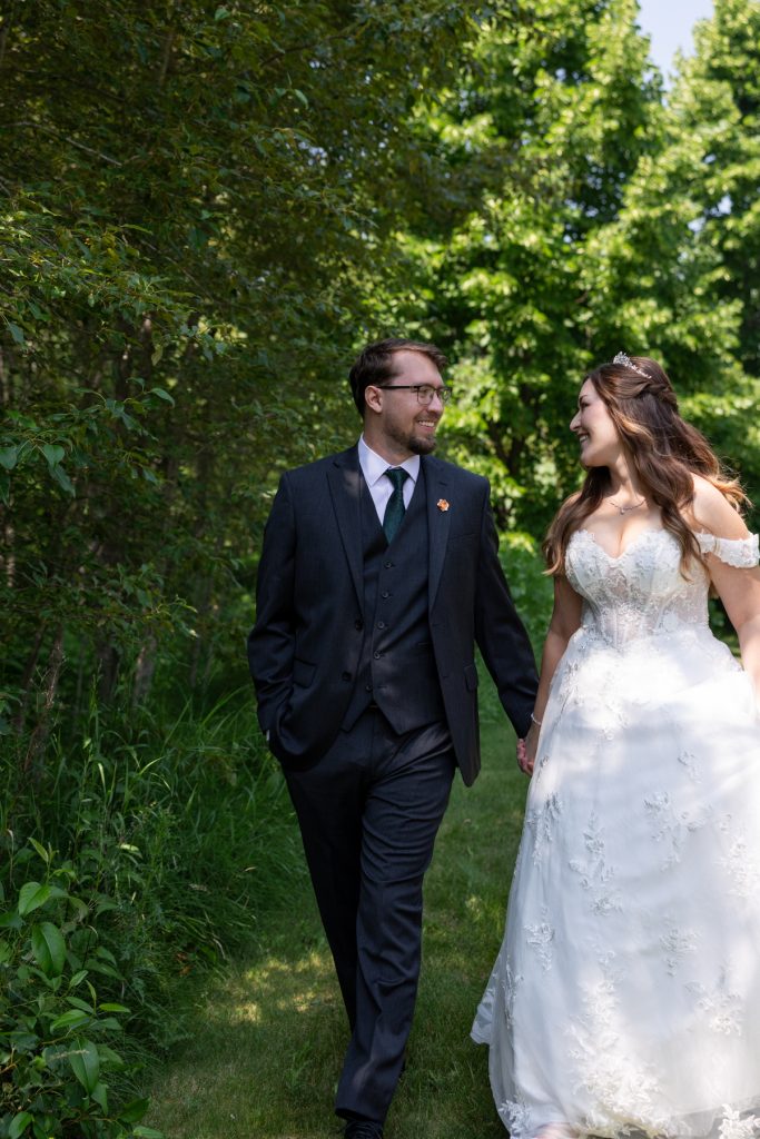 Newly married couple walking hand-in-hand through a wooded area, showcasing Wisconsin wedding photography and videography