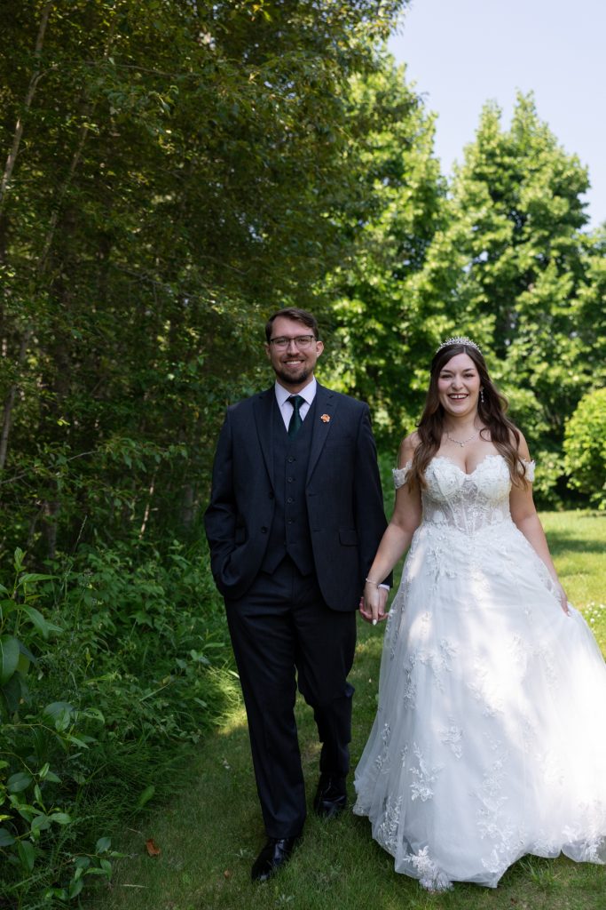 Newly married couple holding hands and walking through a lush green wooded area, showcasing joyful