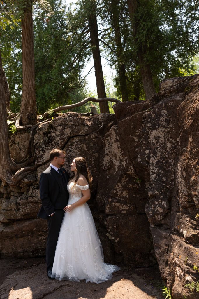 Bride and groom in wedding attire stand embracing against a backdrop of rocky terrain