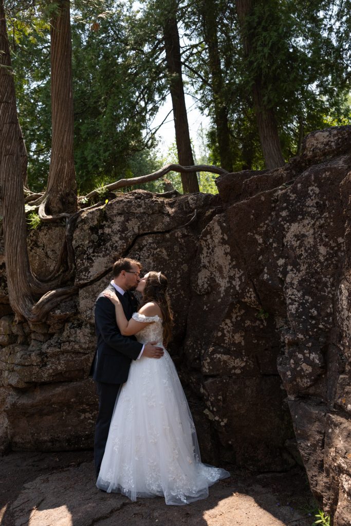 Bride and groom embracing in a romantic wedding portrait set against a backdrop of trees