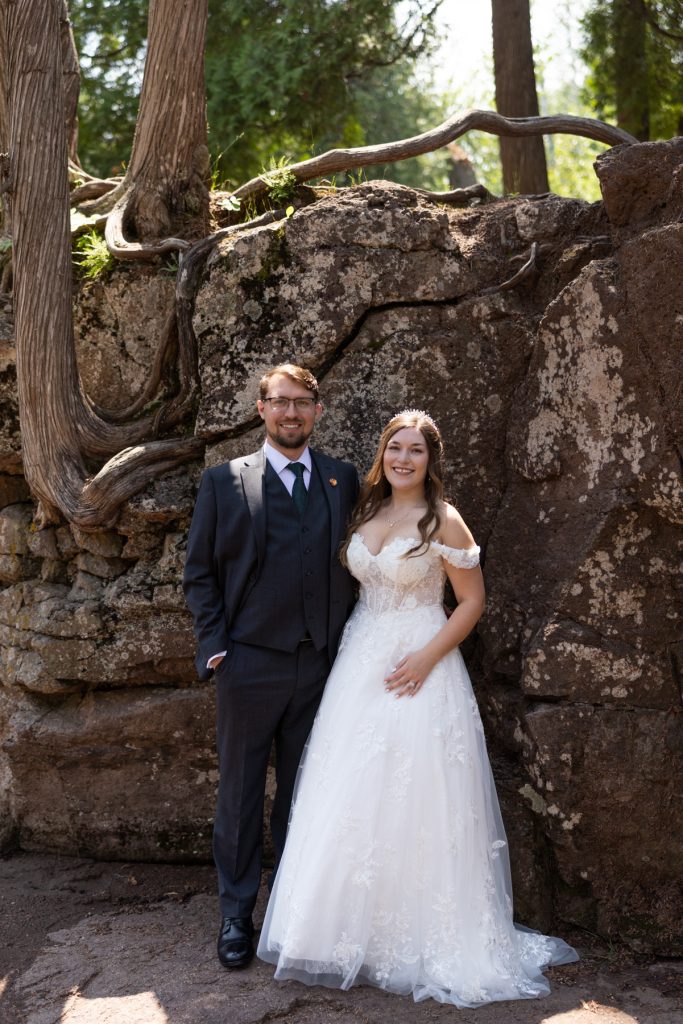 Newly married couple posing for wedding photography near a rocky, wooded area in Wisconsin, showcasing