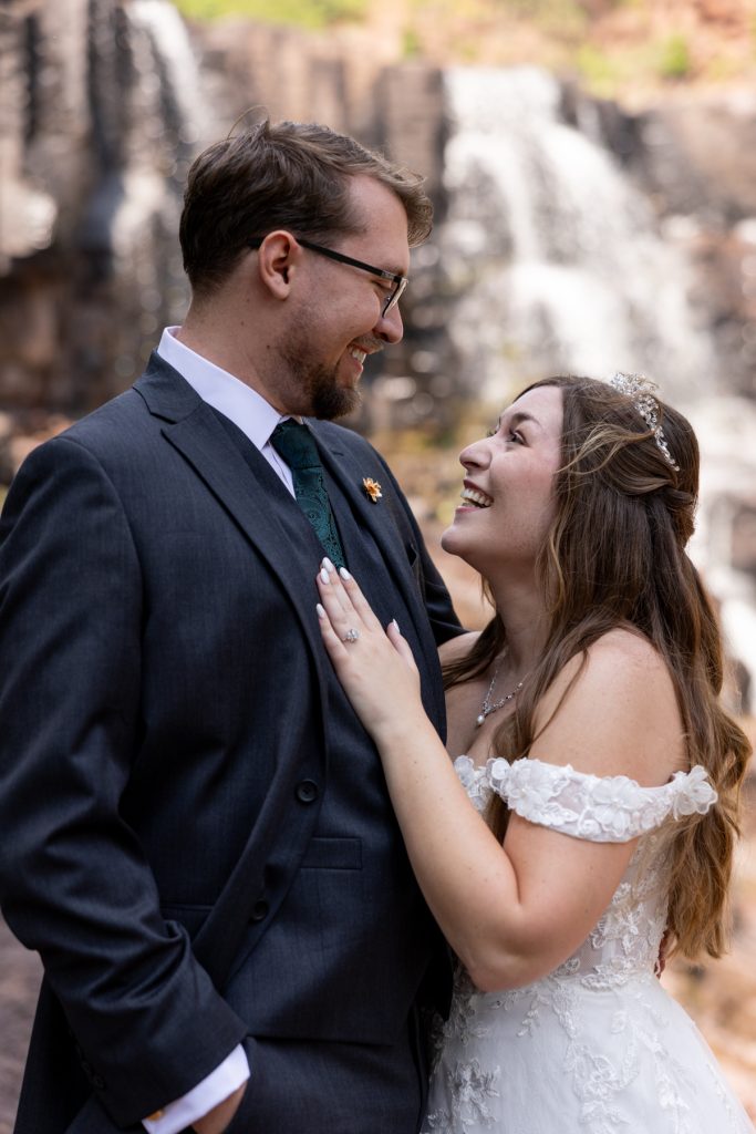 Newly married couple smiles and embraces near a scenic waterfall in Wisconsin, captured by Beau