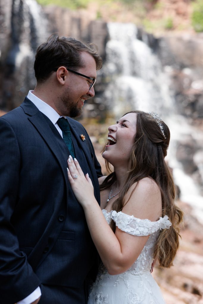 Joyful wedding couple laughingly embracing near a scenic waterfall in Wisconsin, captured by Beau Petersen