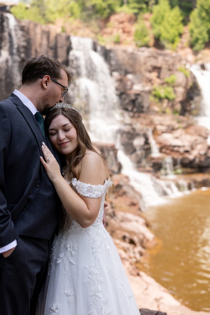 Bride and groom embracing tenderly with a scenic Wisconsin waterfall as a backdrop, captured