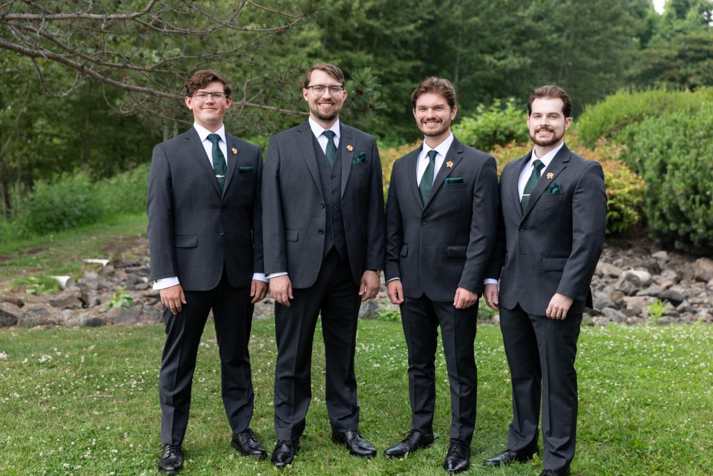 Four groomsmen in dark gray suits and green ties pose outdoors at a Wisconsin wedding