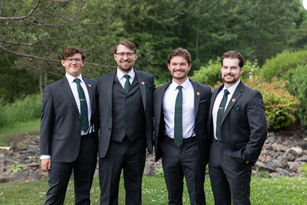 Four groomsmen in matching dark suits and green ties smiling for a wedding portrait