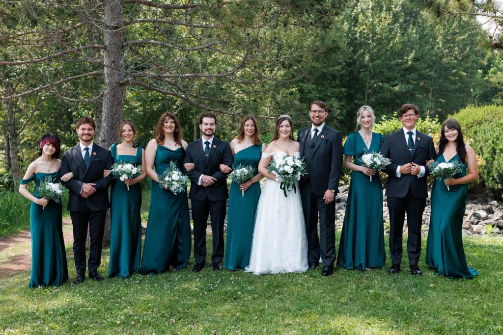 Wedding party portrait featuring a bride and bridesmaids in emerald green dresses and groomsmen