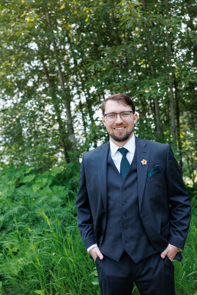 Groom in a navy suit and teal tie, with floral accents, smiles for a wedding