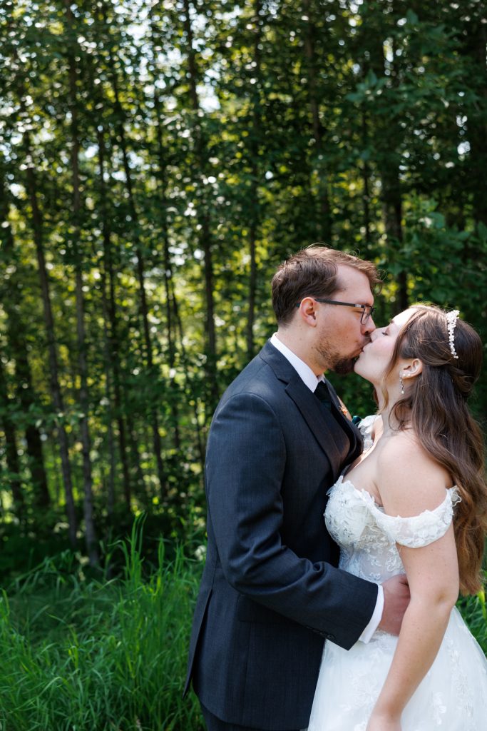 Bride and groom share a romantic kiss in a wooded setting, captured by Beau Petersen