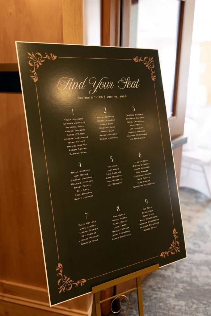 Elegant wedding seating chart displayed on a black board with gold lettering, listing guest names