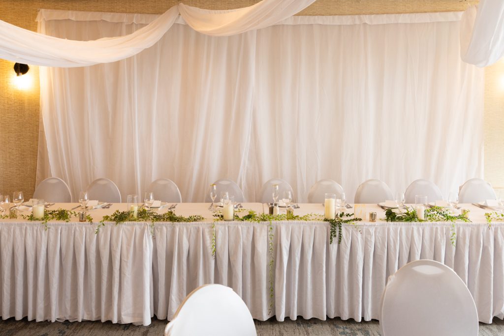 Elegant wedding reception table setup with white draping and greenery, showcasing Beau Petersen Photography's wedding