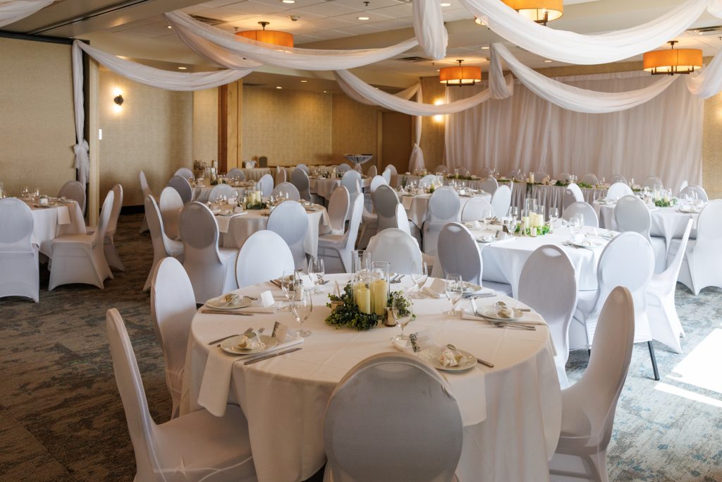 Elegant wedding reception setup with round tables and white chairs, beautifully decorated with flowing white