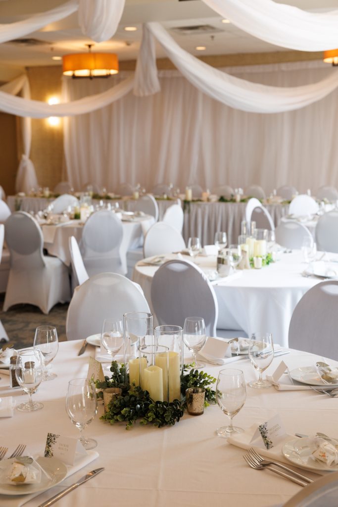 Elegant wedding reception tablescape with white linens, gray chairs, and lush greenery centerpieces, showcasing Beau