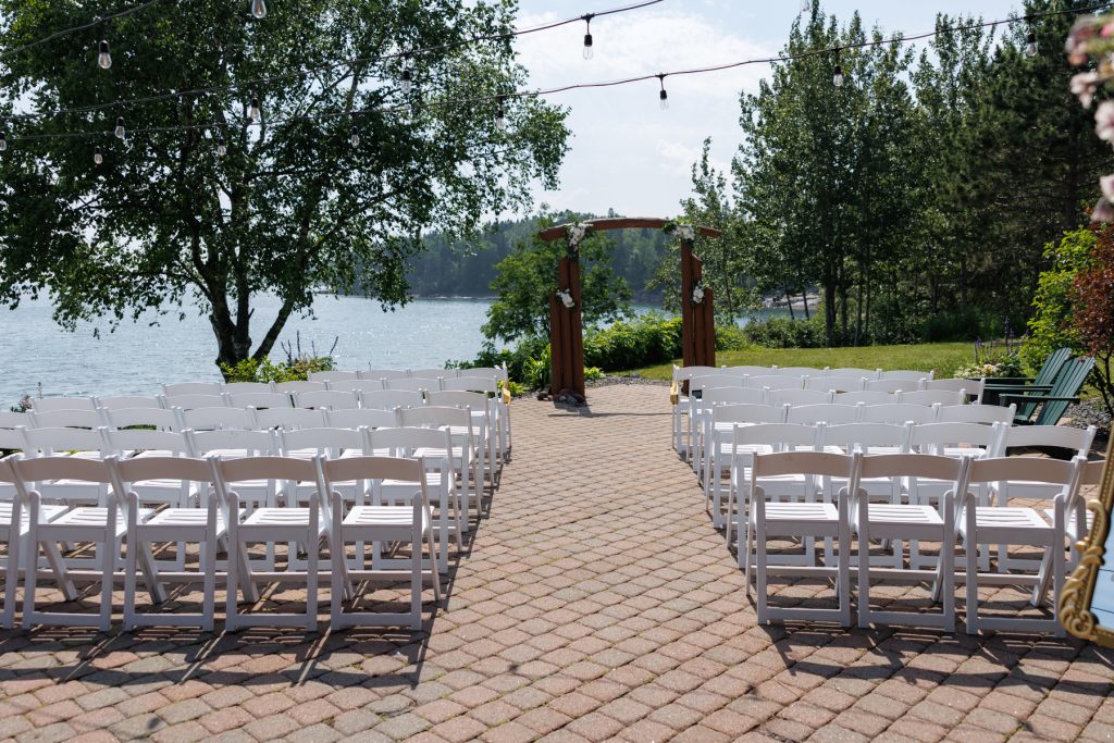 Outdoor wedding ceremony setup with rows of white chairs facing a wooden archway