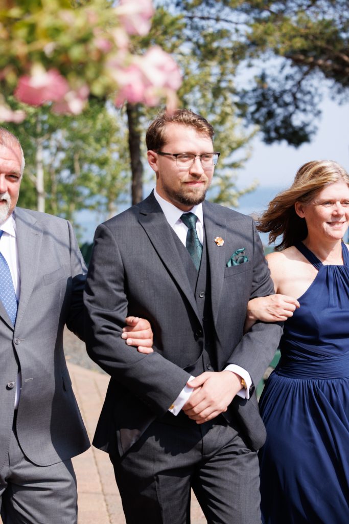 Groom in a dark suit and vest with a green tie and pocket square walks