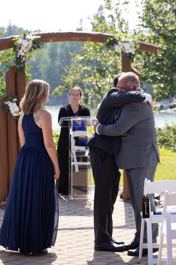 Emotional wedding moment captured by Beau Petersen Photography: Groom embracing his father near a floral