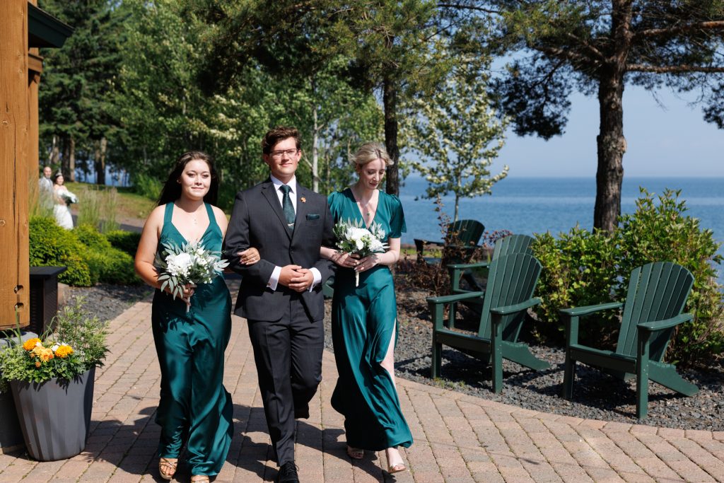 Bride and bridesmaids in emerald green dresses walking along a lakeside path during a Wisconsin