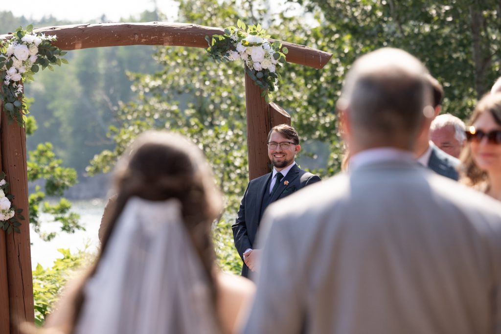 Groom smiling and awaiting his bride beneath a floral arch at a Wisconsin wedding ceremony