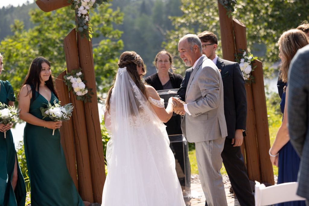 Bride and groom holding hands during their wedding ceremony near a lake in Hayward, Wisconsin
