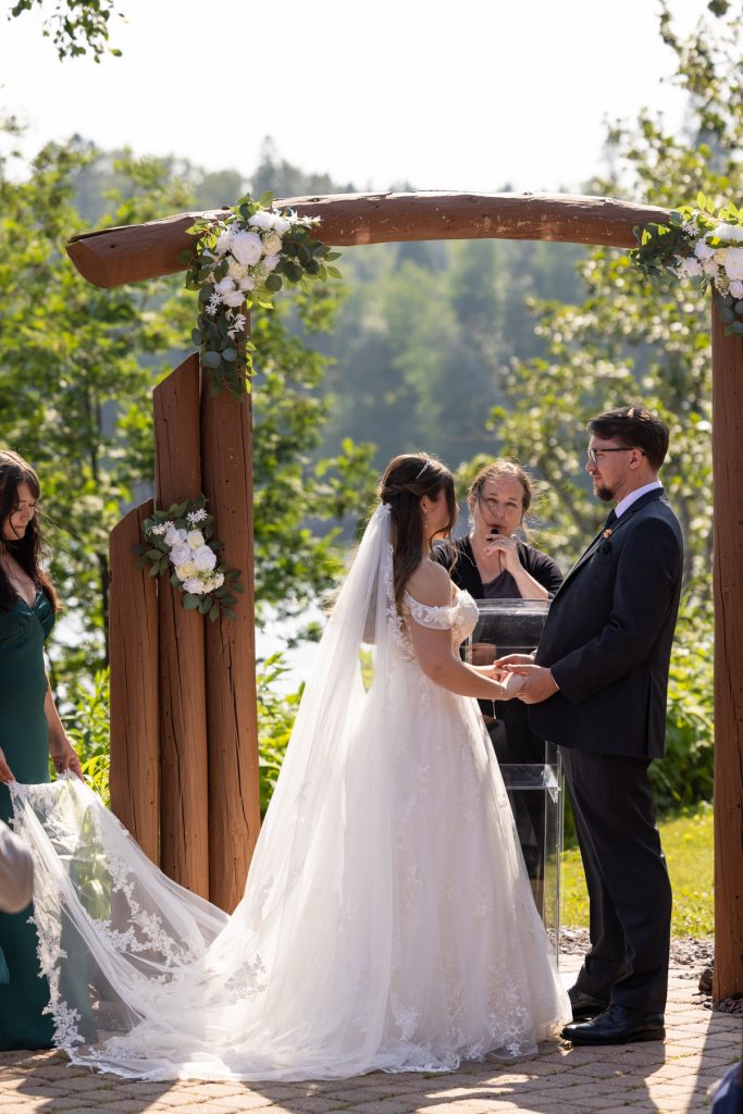 Bride and groom exchanging vows under a floral-adorned wooden archway during a Wisconsin wedding ceremony