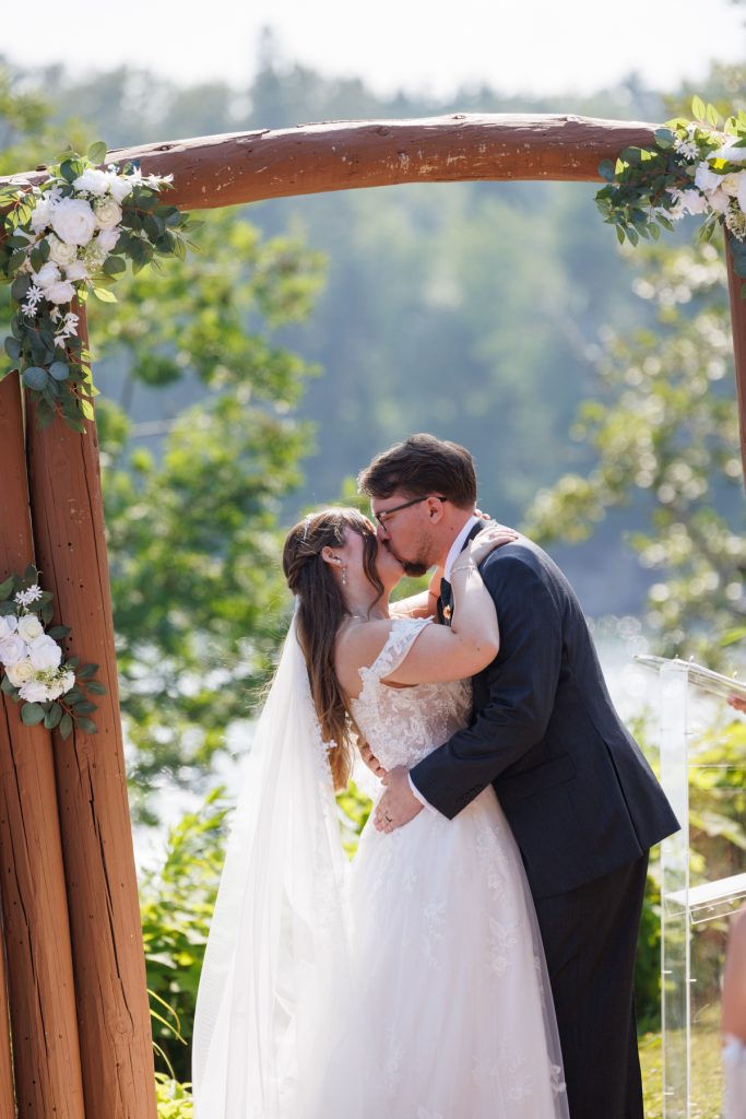 Bride and groom sharing a kiss beneath a wooden floral arch during a Wisconsin wedding