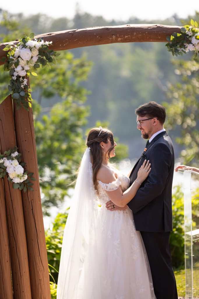 Bride and groom exchange vows under a wooden floral arch during a wedding ceremony