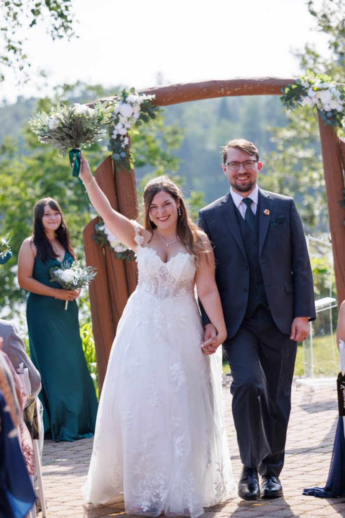 Bride and groom celebrating their wedding day under a floral arch in Hayward, Wisconsin, captured