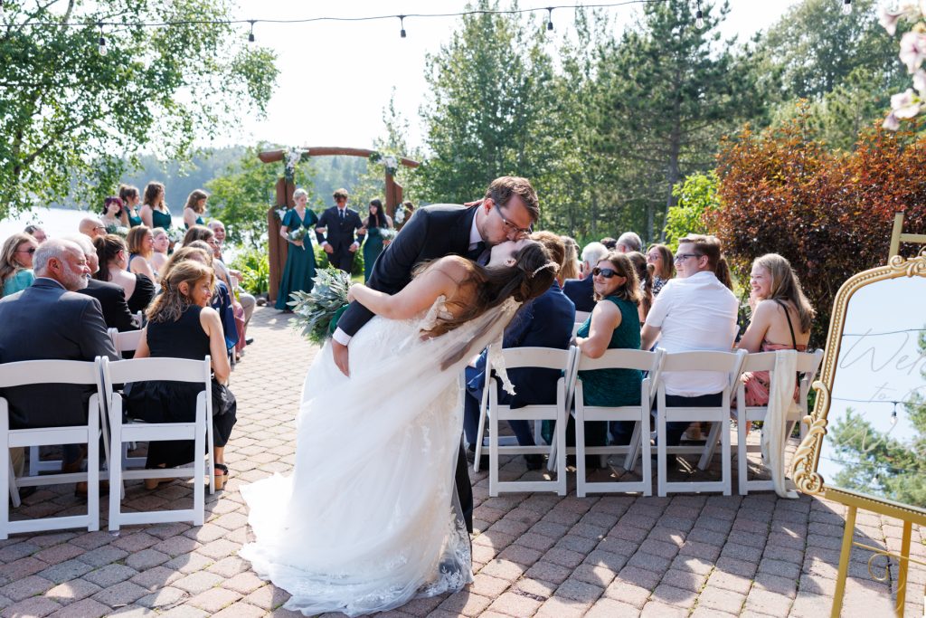 Bride and groom sharing a joyful kiss during an outdoor wedding ceremony near a lake