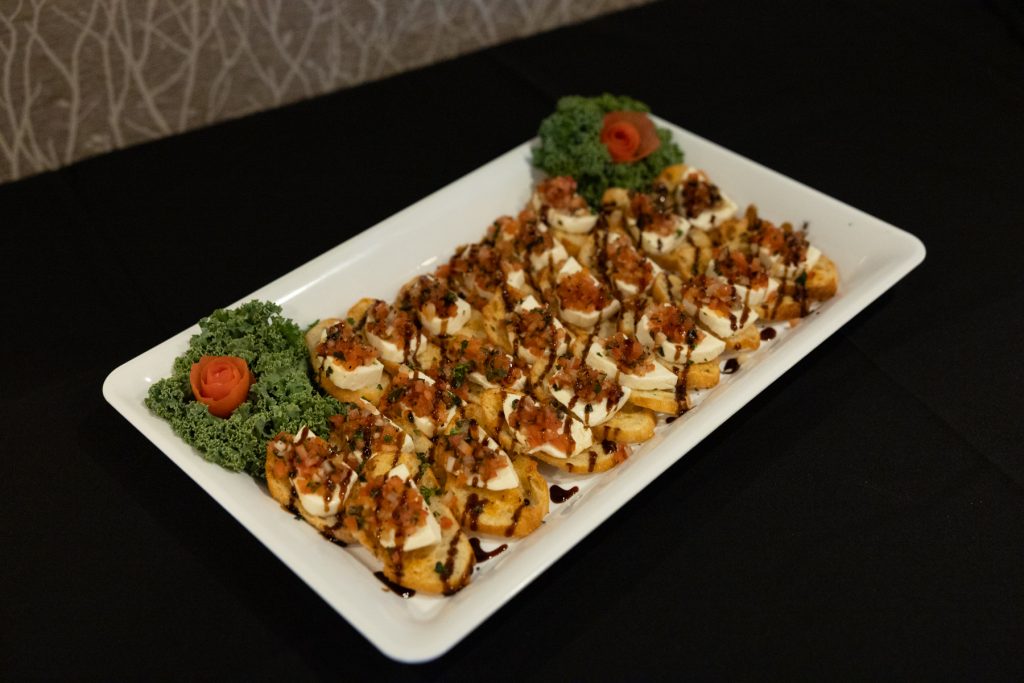 Elegant wedding appetizers displayed on a white platter, featuring bruschetta with ricotta and balsamic glaze
