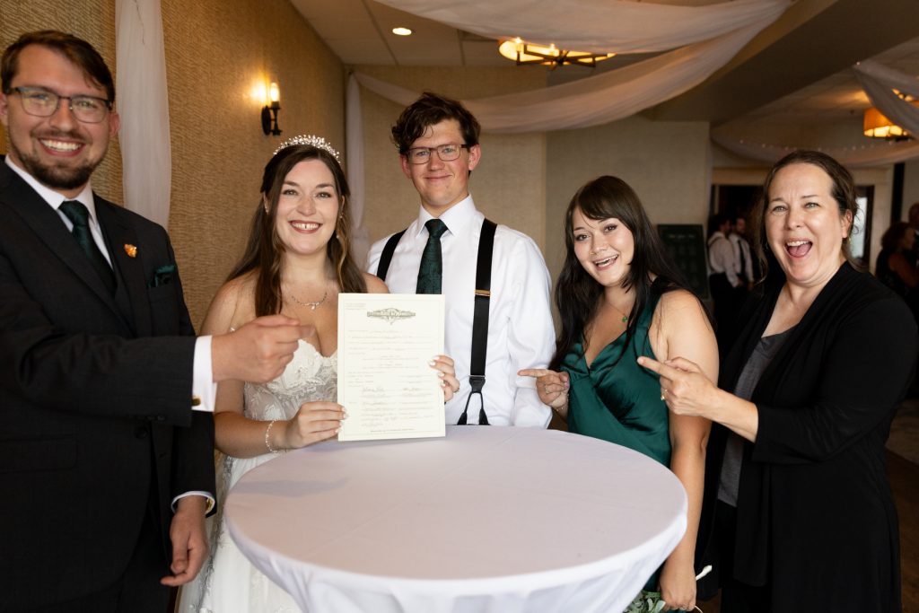 Wedding photography captures a joyful moment with the bride and groom signing their marriage license